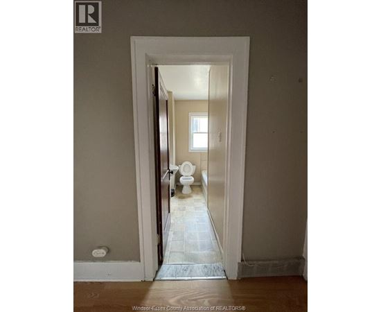 A bathroom with a toilet and a doorway leading to another room.