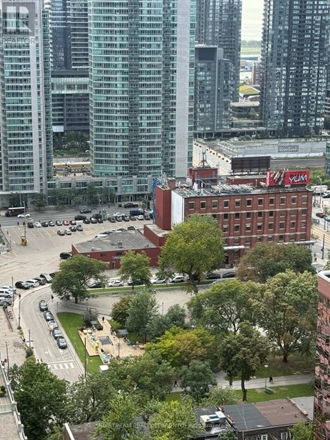 A cityscape with a mix of modern and older buildings, a parking lot, and a tree-lined street.