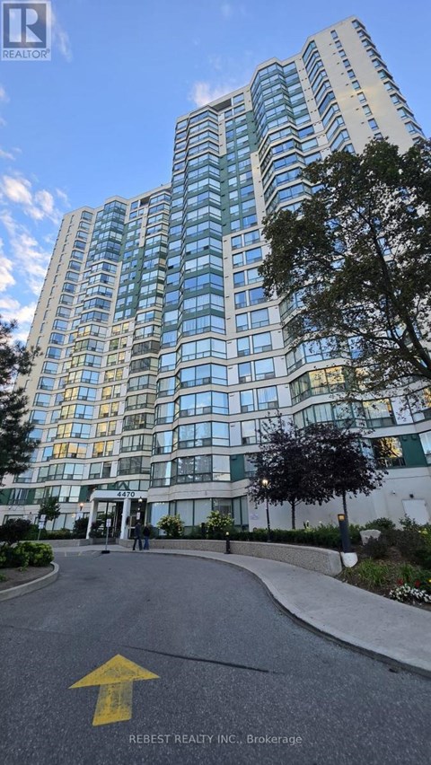 A tall building with many windows is shown with a yellow arrow on the road in front.
