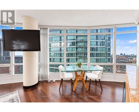 A modern dining room with a glass table and chairs, a flat screen TV, and a view of the city.