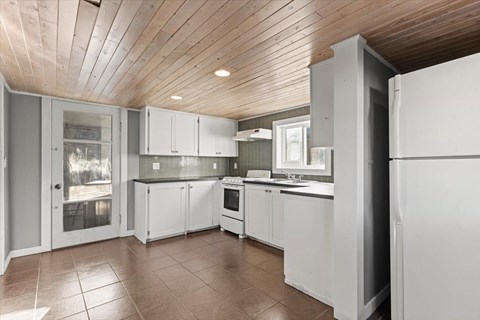 A kitchen with white cabinets and a wooden ceiling.
