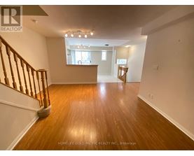 A spacious room with wooden floors and a staircase on the left side.