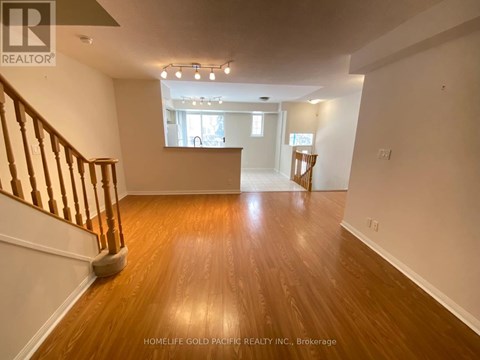 A spacious room with wooden floors and a staircase on the left side.