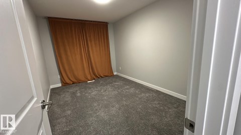 A room with a grey carpet and a brown curtain.