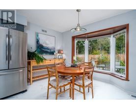 A dining room with a wooden table and chairs, a fridge, and a painting on the wall.