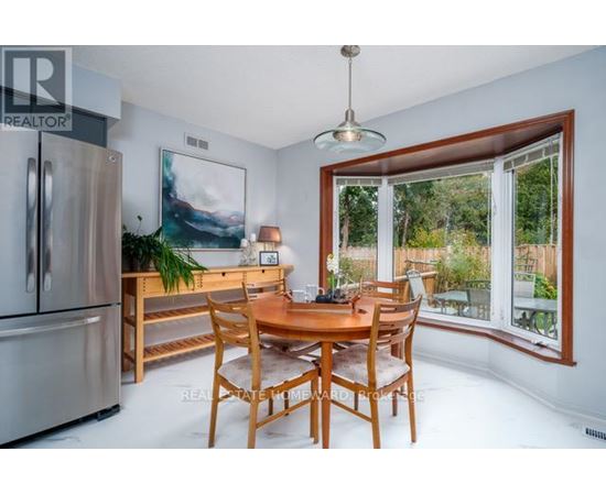 A dining room with a wooden table and chairs, a fridge, and a painting on the wall.