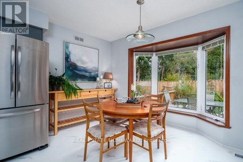 A dining room with a wooden table and chairs, a fridge, and a painting on the wall.