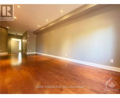 A spacious room with wooden flooring and a hallway leading to another room.