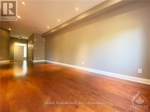 A spacious room with wooden flooring and a hallway leading to another room.