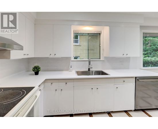 A modern kitchen with white cabinets and a diamond logo on the counter.