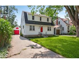 A white house with a red door is surrounded by greenery.