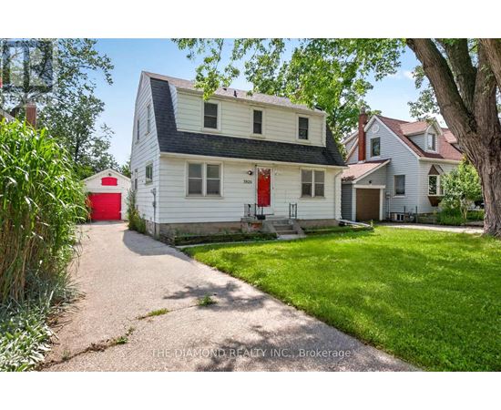A white house with a red door is surrounded by greenery.