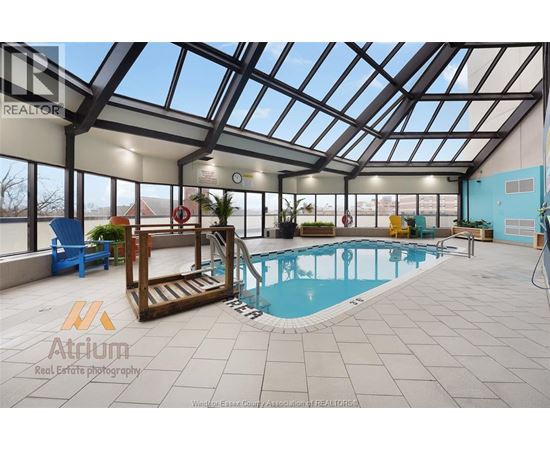 A large indoor swimming pool with a glass ceiling and a wooden staircase leading to it.