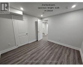 A second bedroom with wood flooring and white walls.