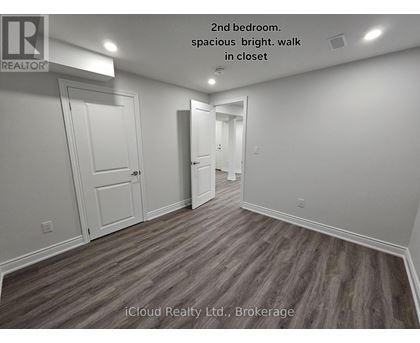 A second bedroom with wood flooring and white walls.