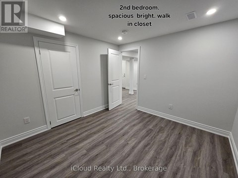 A second bedroom with wood flooring and white walls.