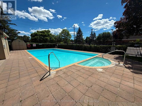 A pool surrounded by a brick patio and a black fence.