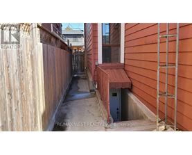 A narrow alley with a wooden fence on the left and a red building on the right.