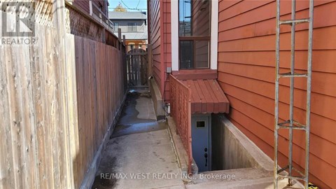 A narrow alley with a wooden fence on the left and a red building on the right.