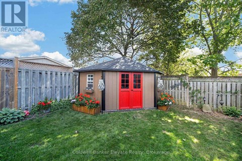 A red shed with a black roof is surrounded by a wooden fence and green grass.