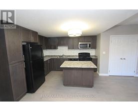 A kitchen with a black fridge and microwave, brown cabinets, and a marble island.