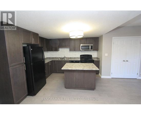 A kitchen with a black fridge and microwave, brown cabinets, and a marble island.