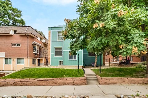 A green house is situated between a red brick house and a tree with orange flowers.