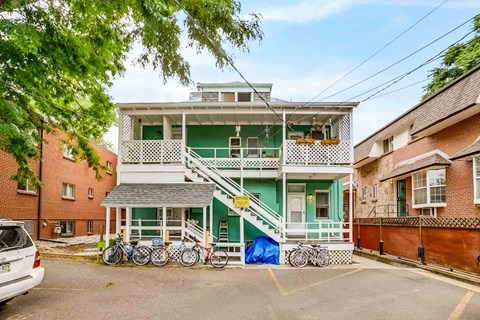 A white and green two-story house with a car parked in front.