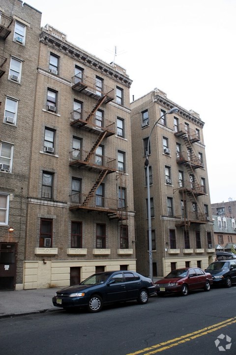 A black car is parked in front of a tan building with a fire escape.