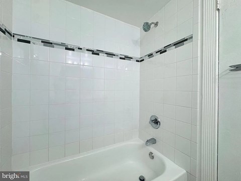 A white bathroom with a white tub and white tiles.