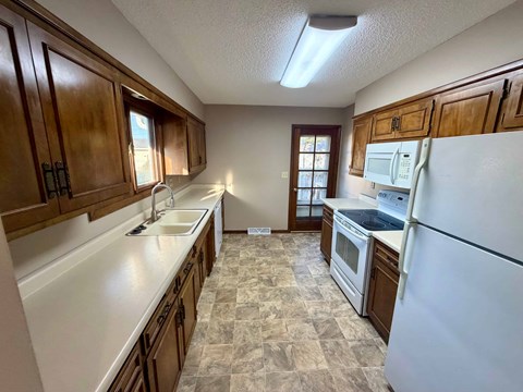 A kitchen with a white refrigerator, brown cabinets, and a tiled floor.