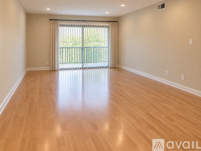 A spacious room with wooden flooring and a sliding glass door.