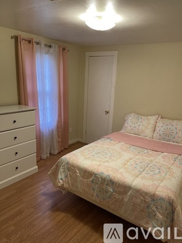 A bedroom with a bed, dresser, and window with curtains.