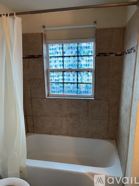 A bathroom with a tub, toilet, and a window with a blue tint.