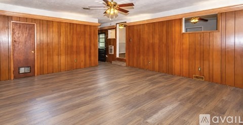 A spacious room with wooden walls and flooring, a ceiling fan, and a television.