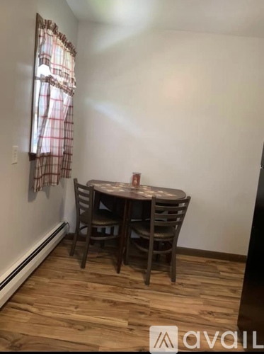 A small table with four chairs is in a room with wooden floors and a window with a red and white checkered curtain.