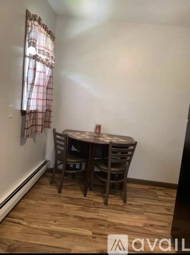A small table with four chairs is in a room with wooden floors and a window with a red and white checkered curtain.