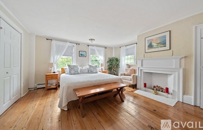 A bedroom with a large bed, a bench, and a fireplace.