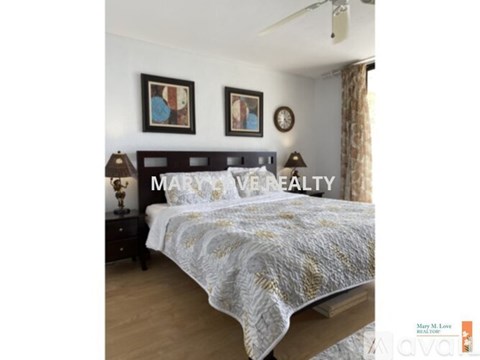 A bedroom with a bed, two pictures on the wall, and a lamp on the nightstand.