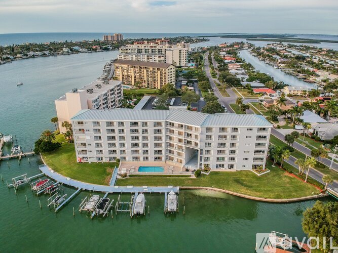 A large white building with a pool in front is surrounded by water and boats.
