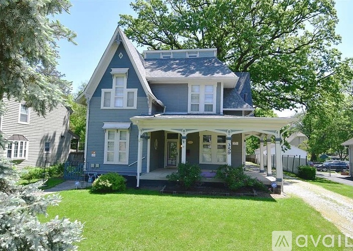 A blue house with a white porch and a tree in front.