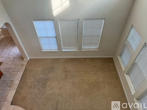A room with a tan carpet and three windows with blinds.