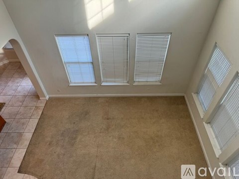A room with a tan carpet and three windows with blinds.