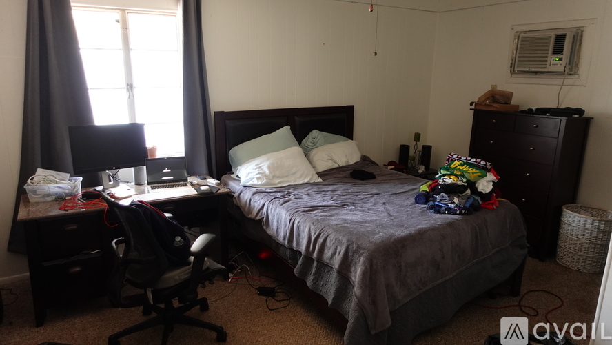 A bedroom with a bed, desk, chair, and window.