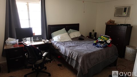 A bedroom with a bed, desk, chair, and window.