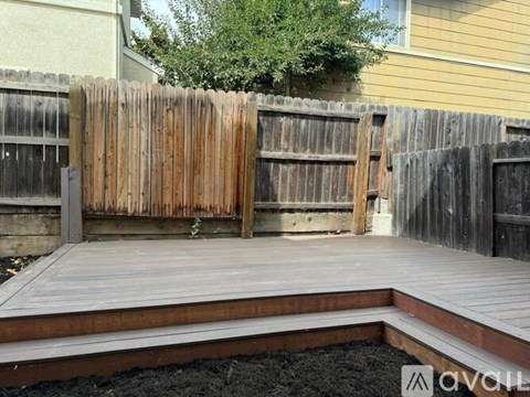 A wooden deck with a brown fence and a small tree in the background.