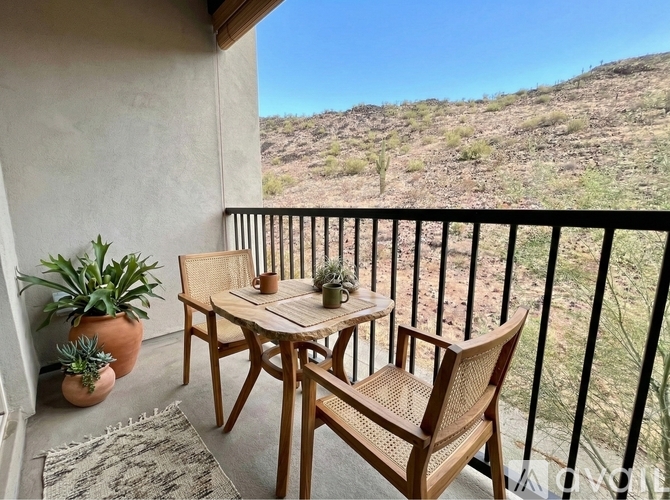 A balcony with a table and chairs overlooking a desert landscape.