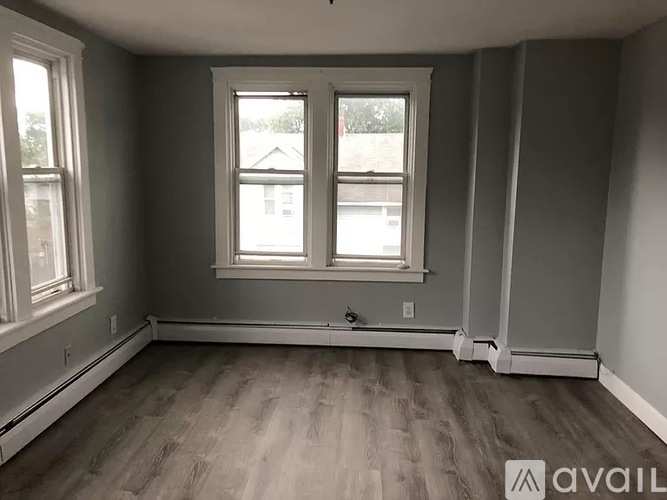 A room with grey walls and wooden flooring, featuring a window with white frames.