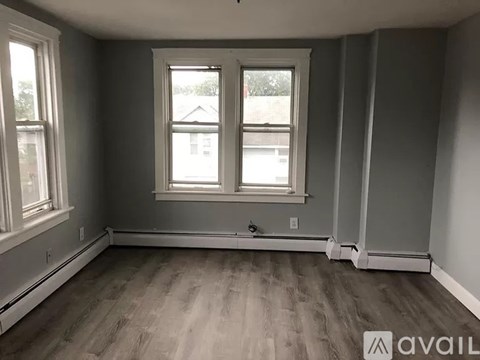 A room with grey walls and wooden flooring, featuring a window with white frames.