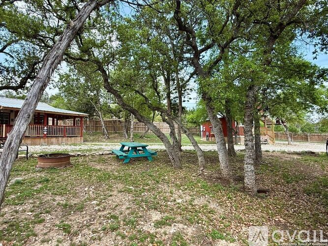 A green picnic table is in the middle of a yard with trees.